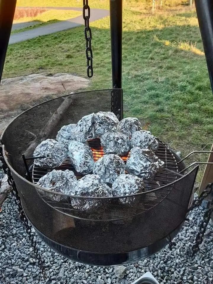 potatoes wrapped in tin foil are cooking on a grill .