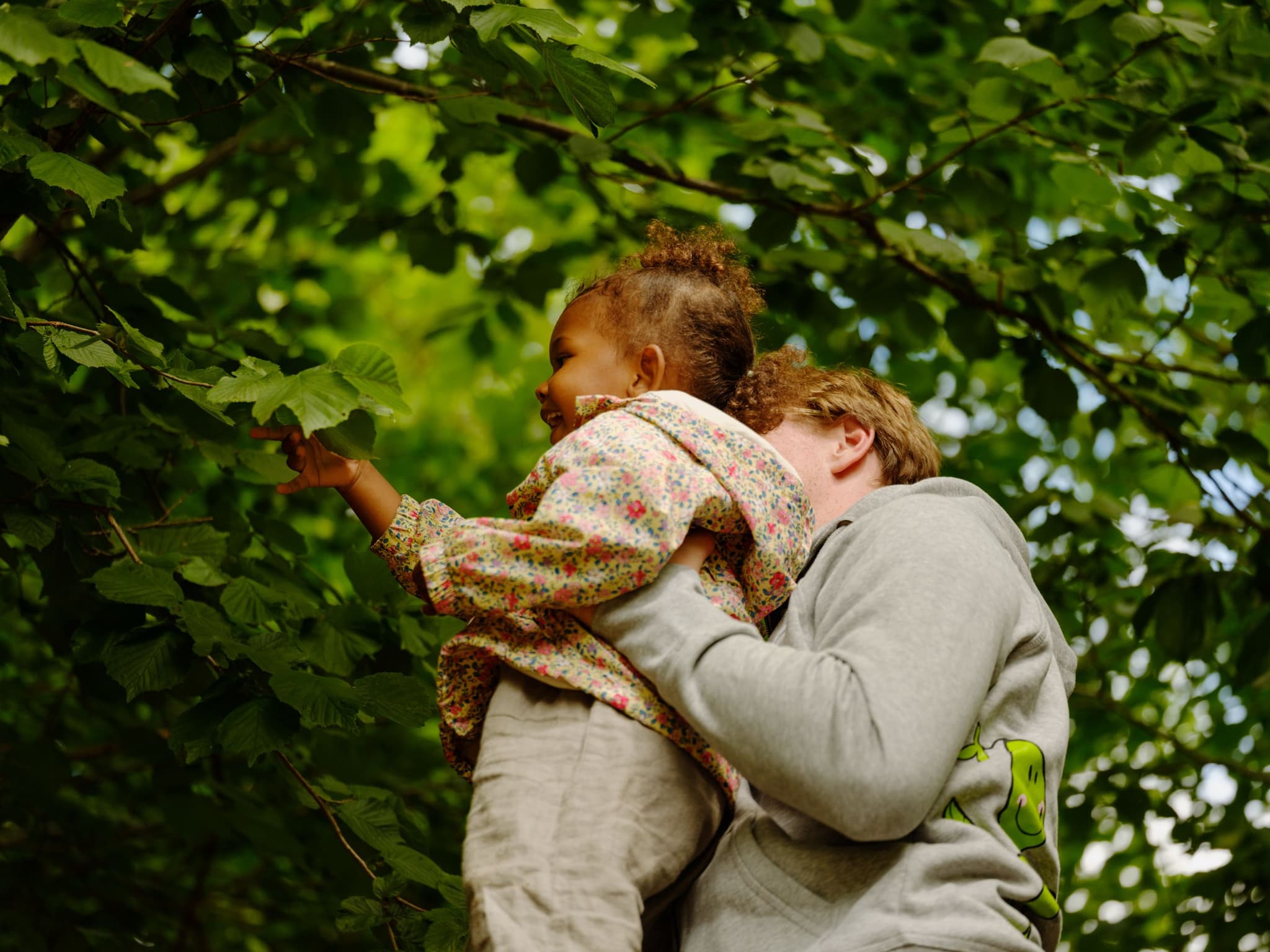 a man is holding a little girl in his arms while she climbs a tree .