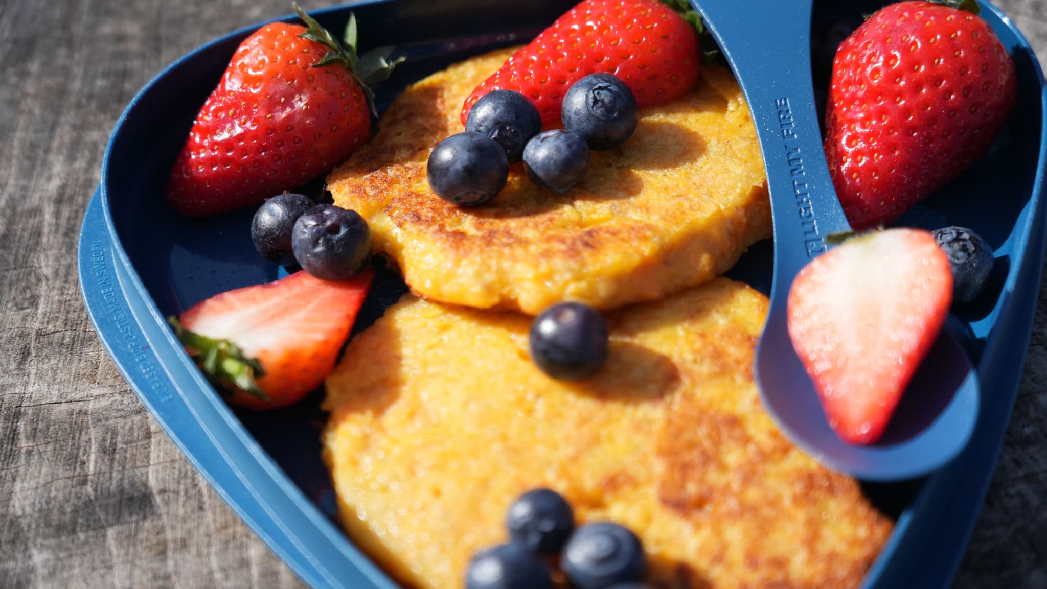 a blue plate topped with pancakes , strawberries , blueberries and a spoon .