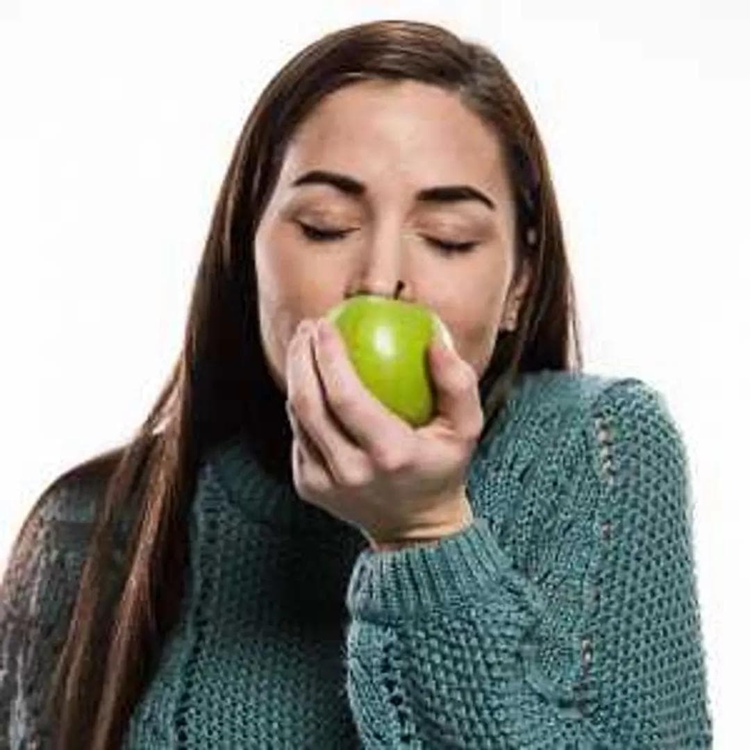 a woman is eating a green apple with her eyes closed .